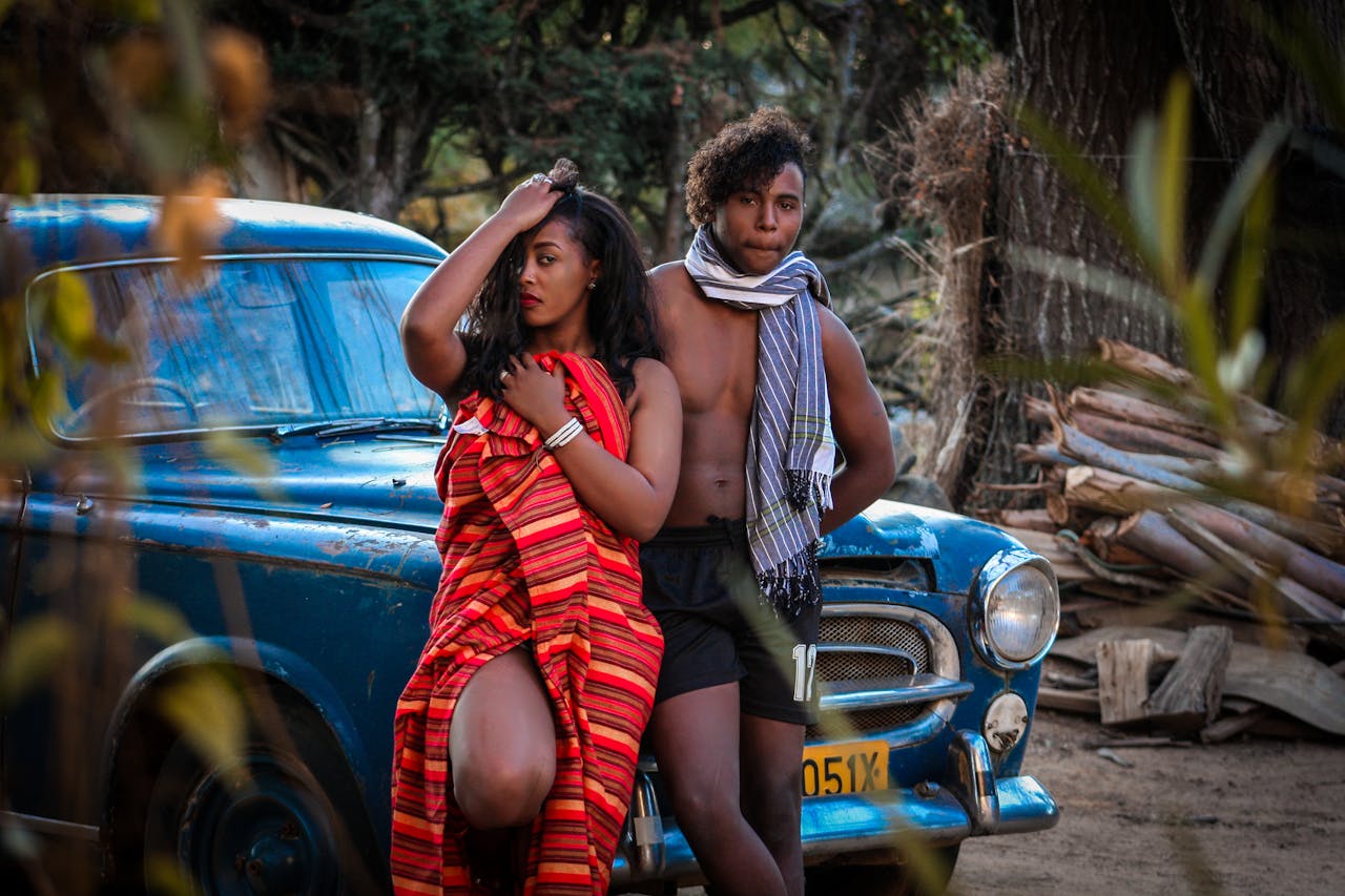 Stylish young couple posing against a vintage car in a natural outdoor setting, exuding a vibrant and modern lifestyle.