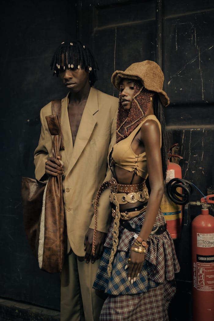 Fashionable duo posing with fire extinguishers in rustic urban setting.